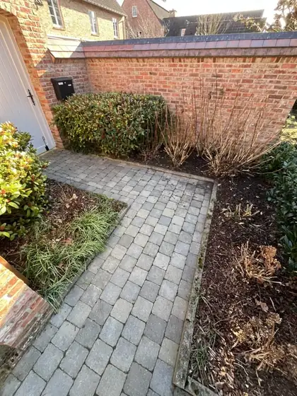 Allée pavée bordée de deux parterres nettoyés, devant un mur en briques